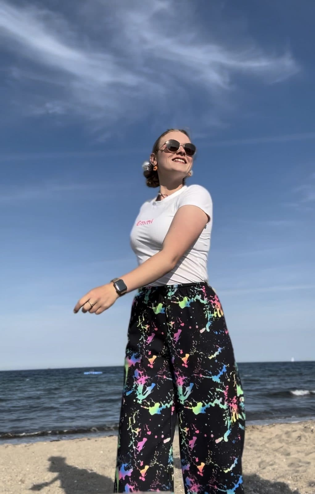 Emmi am Ostseestrand in bunt bespritzter Hose und Emmi's-Shirt