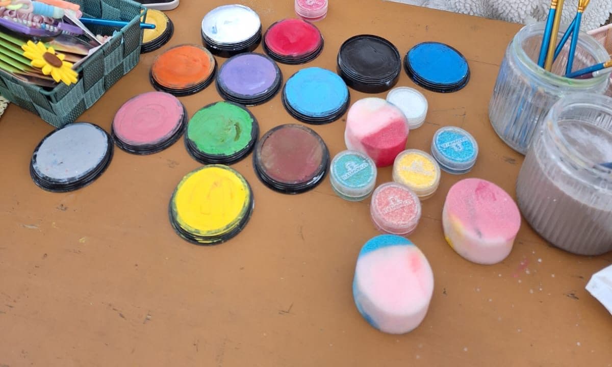 Bunte Schminkfarben, Glitzerdosen und Pinsel auf einem Holztisch
